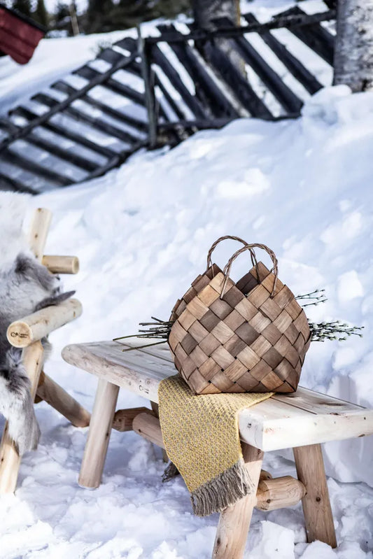 Log benk med kurv og pledd plassert i snøen ved et gjerde