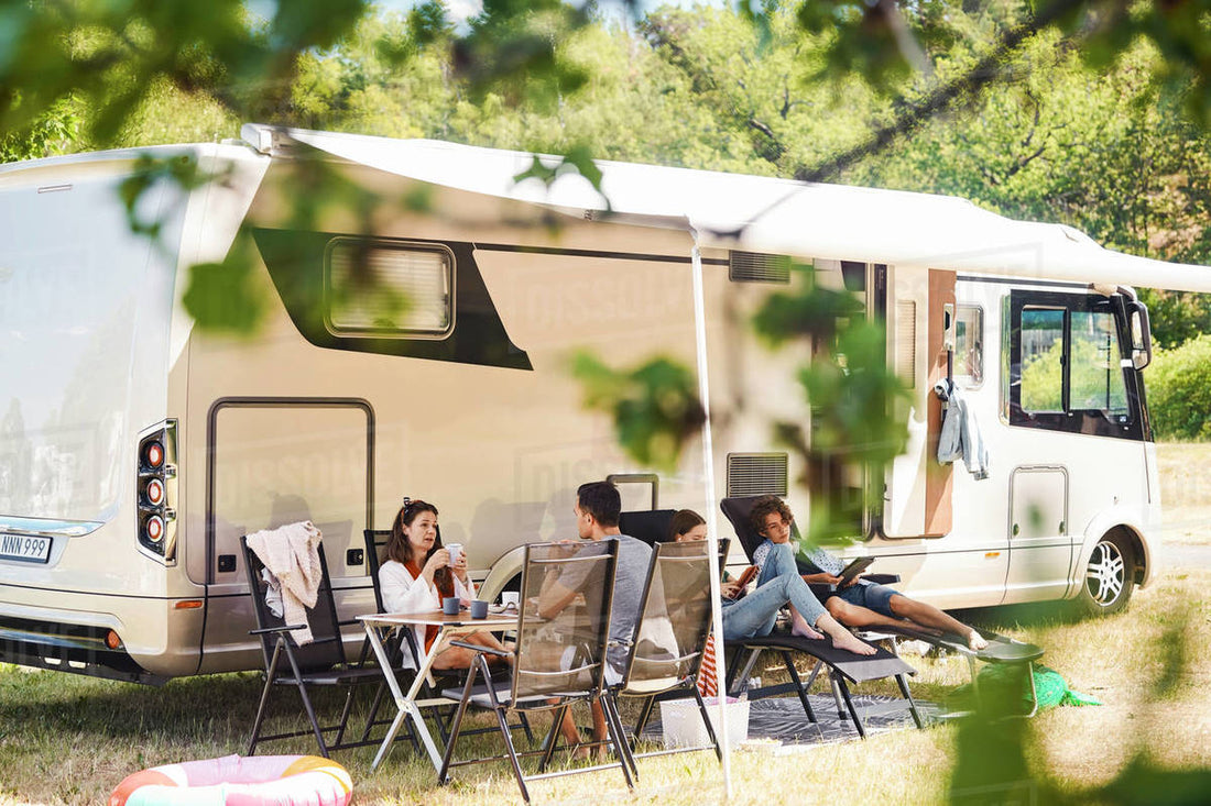 familie sittende i campingstoler utenfor en bobil med markise ute