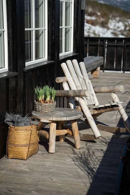 Log sidebord med påskeliljer i en kurv olassert på bordet, ved siden av en log stol  på en hytteterasse