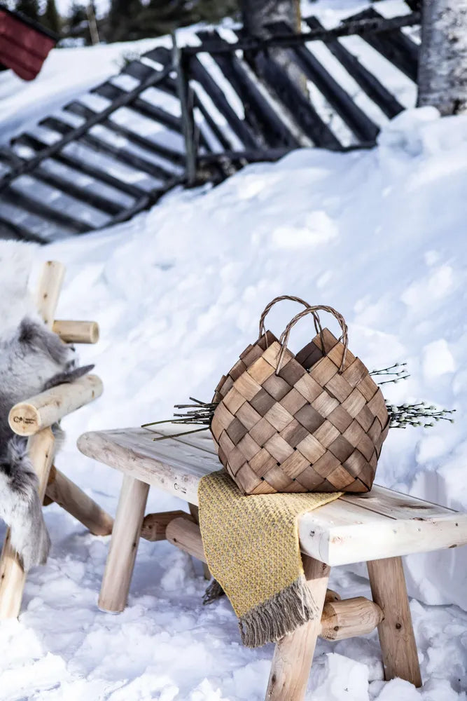 Log benk  med kurv og pledd plassert i snøen ved et gjerde